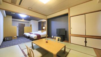 A hotel room with a bed, a TV, a desk, and a traditional Japanese tatami mat floor.