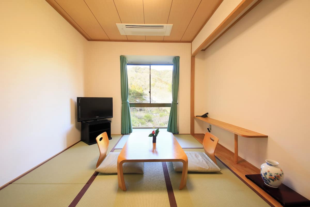 A traditional Japanese room with tatami flooring, a low table with a vase, a television, and a window with curtains.