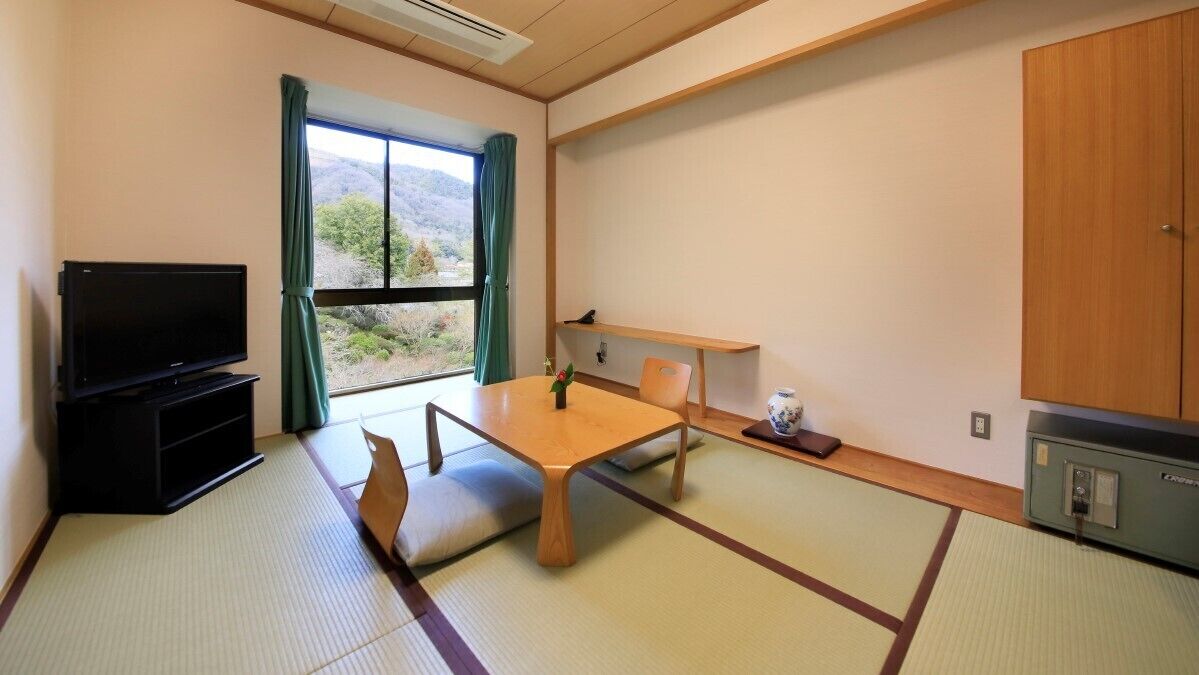 A room with tatami flooring, a television, a table with chairs, a cabinet, and a view of the outdoors.