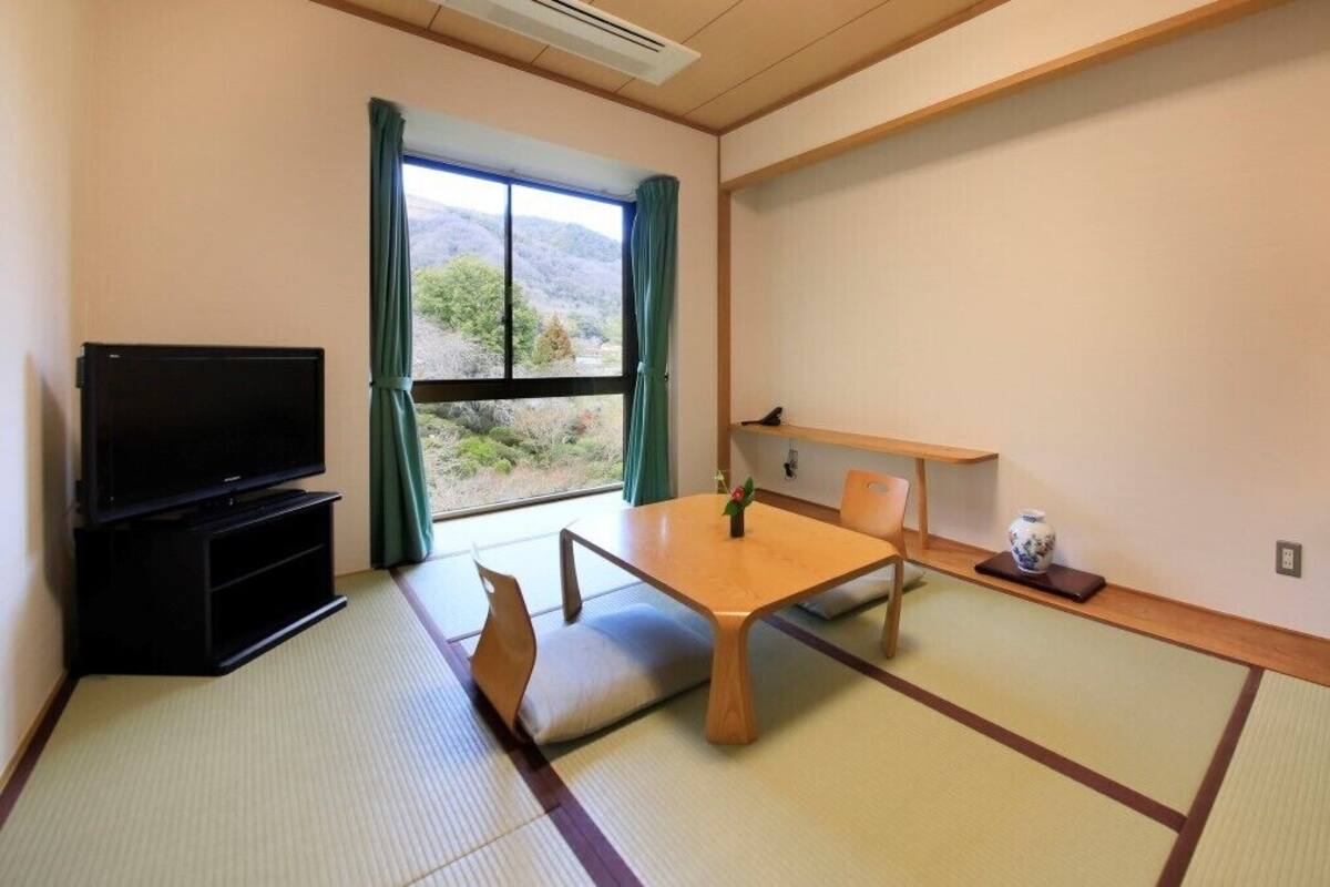 A room with tatami flooring, a television, a table with chairs, a cabinet, and a view of the outdoors.