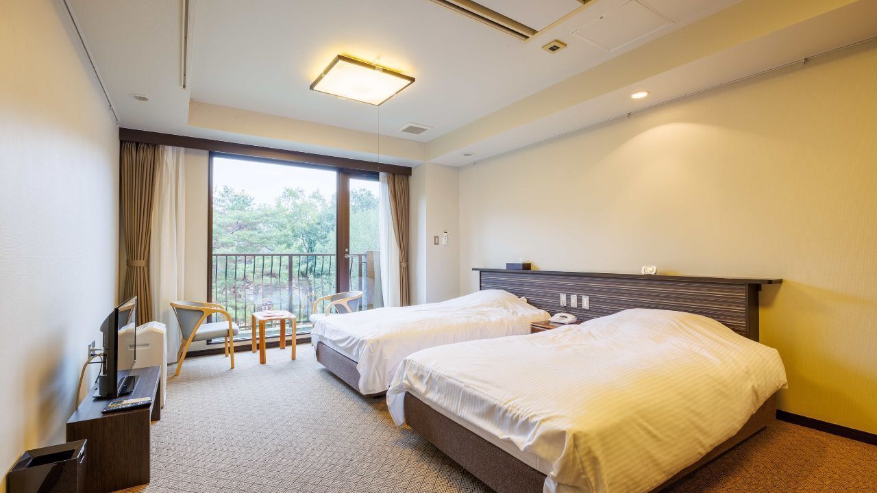 A hotel room with two beds, a desk with a computer, a chair, and a balcony with a view.