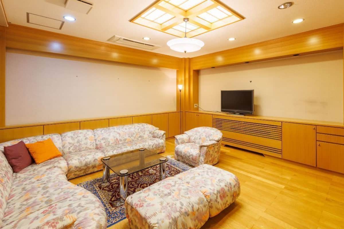 A living room with a sectional sofa, ottoman, and a flat-screen TV.