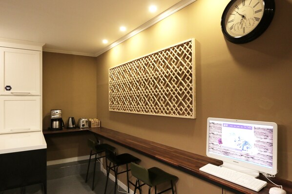 A modern kitchen with a built-in coffee maker, a clock, and a computer on a desk.