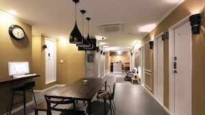 A hotel corridor with a dining area featuring a long table and chairs, a clock on the wall, and a computer monitor on a desk. - Blueboat Hostel Gyeongju (Gyeongju)