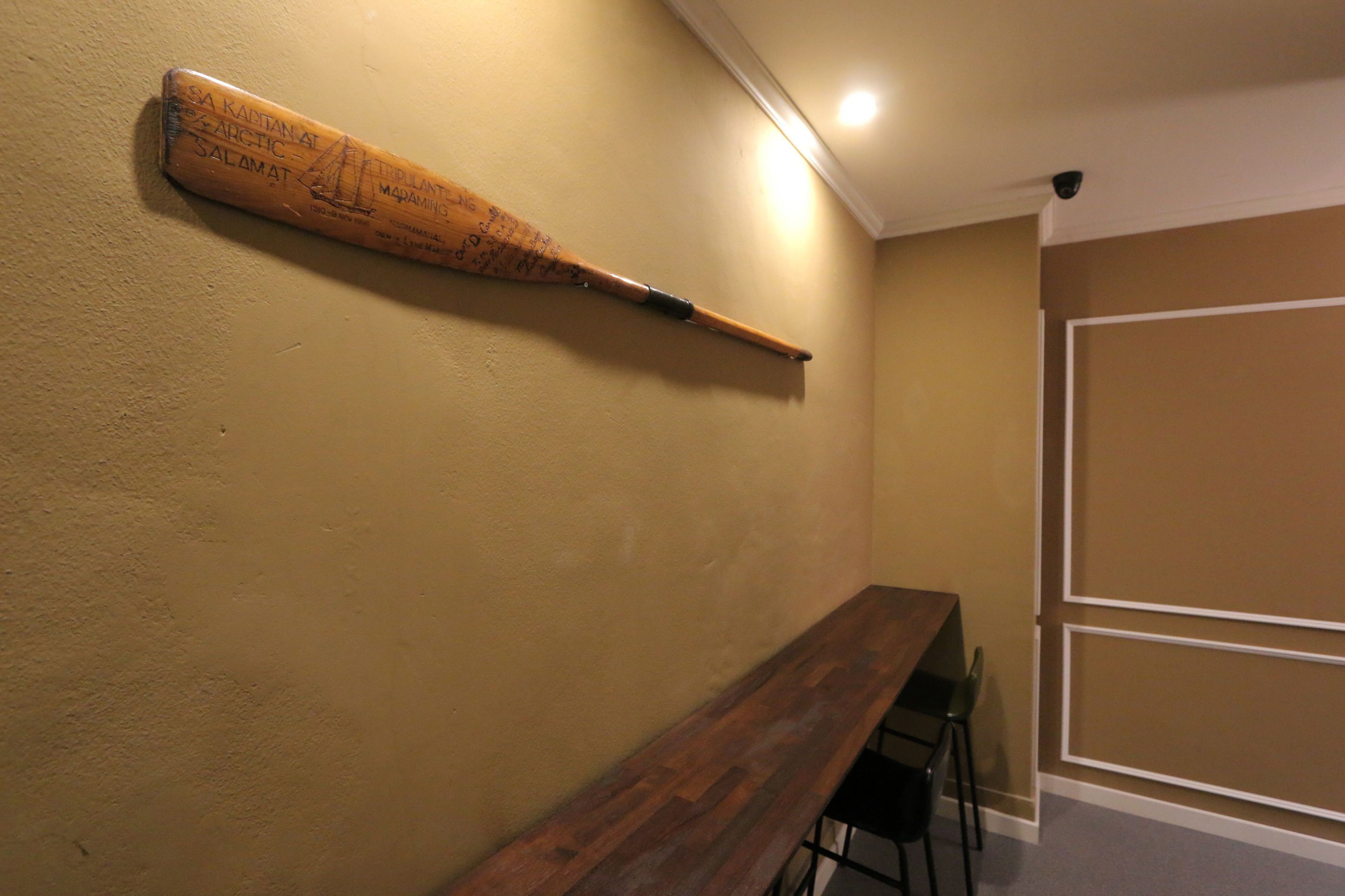 Una habitación con un bate de madera montado en la pared, una larga mesa de madera y dos sillas.