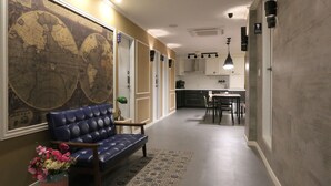A hallway with a blue leather sofa, a large world map on the wall, and a kitchen area in the background. - Blueboat Hostel Gyeongju (Gyeongju)