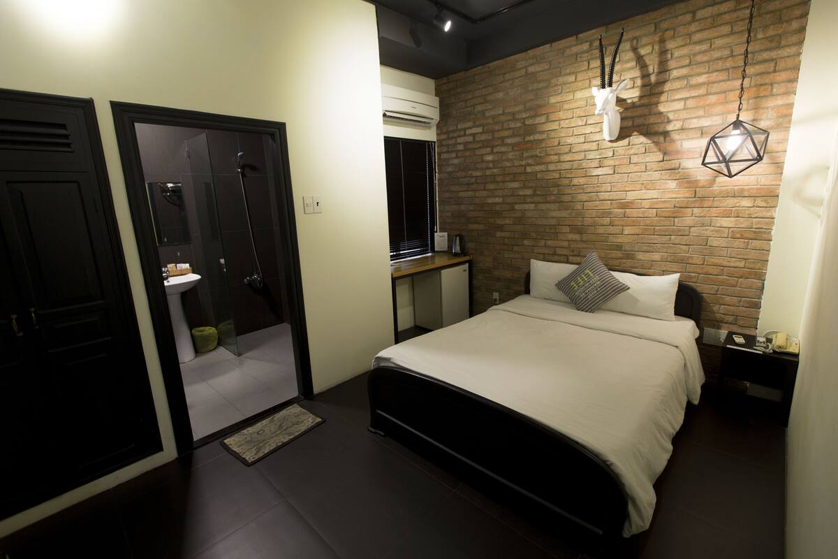 A bedroom with a brick wall, a bed, a nightstand, and a hanging light fixture.