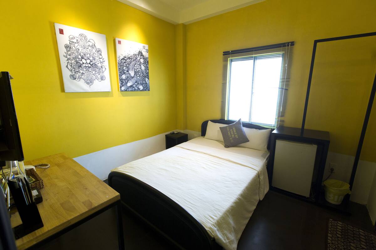 A room with a bed, a desk, and two wall-mounted artworks.