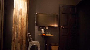 A room with a wooden partition, a television mounted on the wall, a small table with a kettle, a chair, and a wicker basket on the floor. - A in Hotel (Ho Chi Minh City)