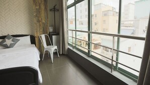 A hotel room with a large window, a bed with white bedding, a chair, and a herringbone-patterned wall. - A in Hotel (Ho Chi Minh City)