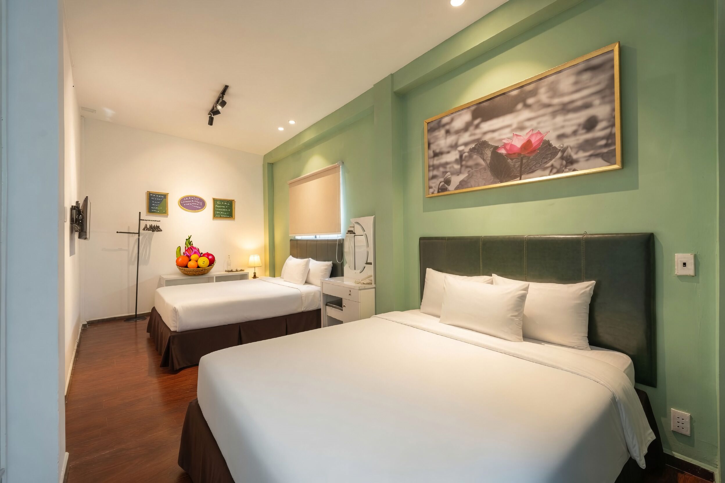 Ein Hotelzimmer mit zwei Betten, einer Obstschale, einem Spiegel und einem gerahmten Bild an der Wand.