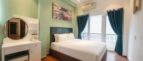 Habitación de hotel con cama, escritorio con espejo, un cuadro en la pared y balcón con cortinas.