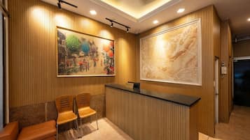 Un área de recepción con pared de paneles de madera, un mostrador de recepción, dos sillas de madera y una obra de arte grande enmarcada.