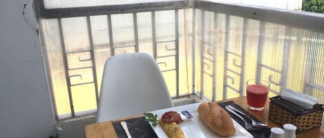 Un balcón con una mesa dispuesta para el desayuno, que incluye un plato con huevos, un panecillo y un vaso de jugo.