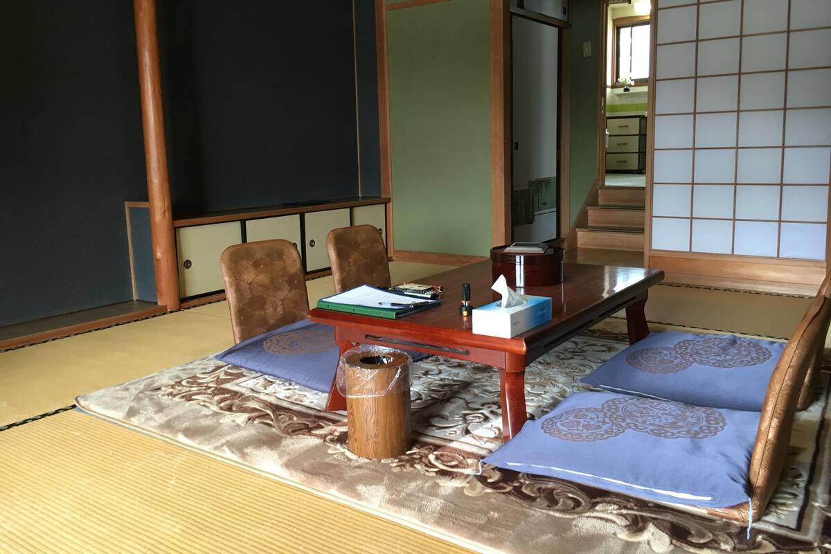 A tatami mat room with a low table, chairs, a waste bin, and a sliding door.