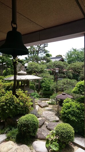 Un jardin japonais traditionnel agrémenté de lanternes en pierre, d’une table en pierre et de divers arbustes.