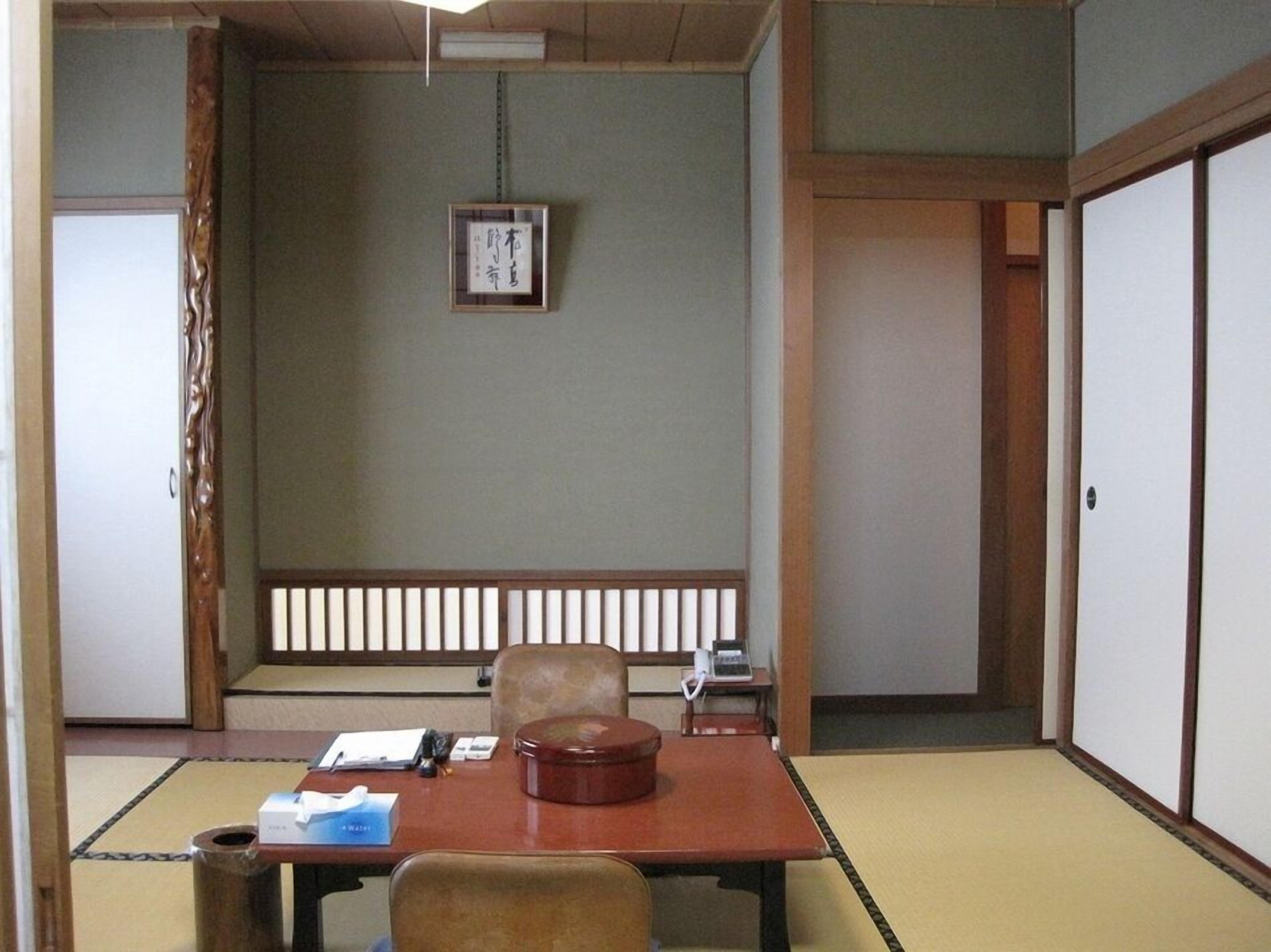 A traditional Japanese room with tatami flooring, a low table, a cushioned chair, and a sliding door.