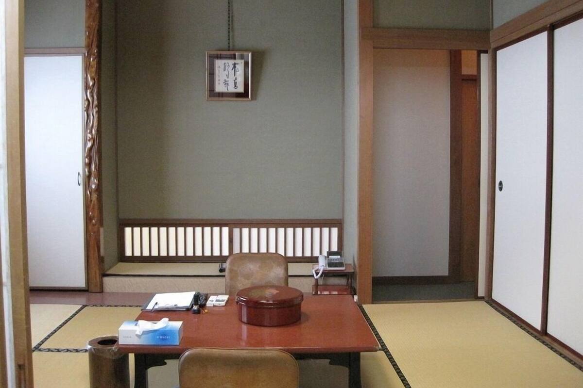 A traditional Japanese room with tatami flooring, a low table, a cushioned chair, and a sliding door.