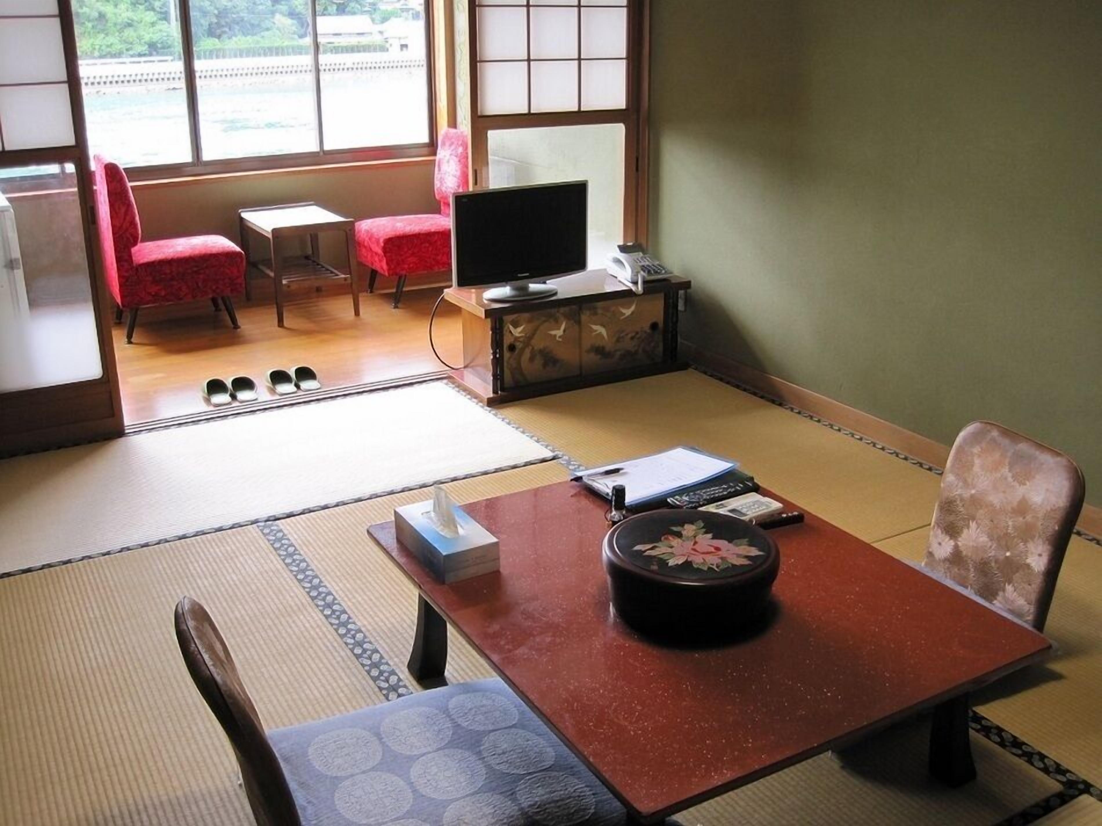 Una habitación de estilo japonés tradicional con suelo de tatami, una mesa baja de tatami, un televisor, un armario y una silla roja.