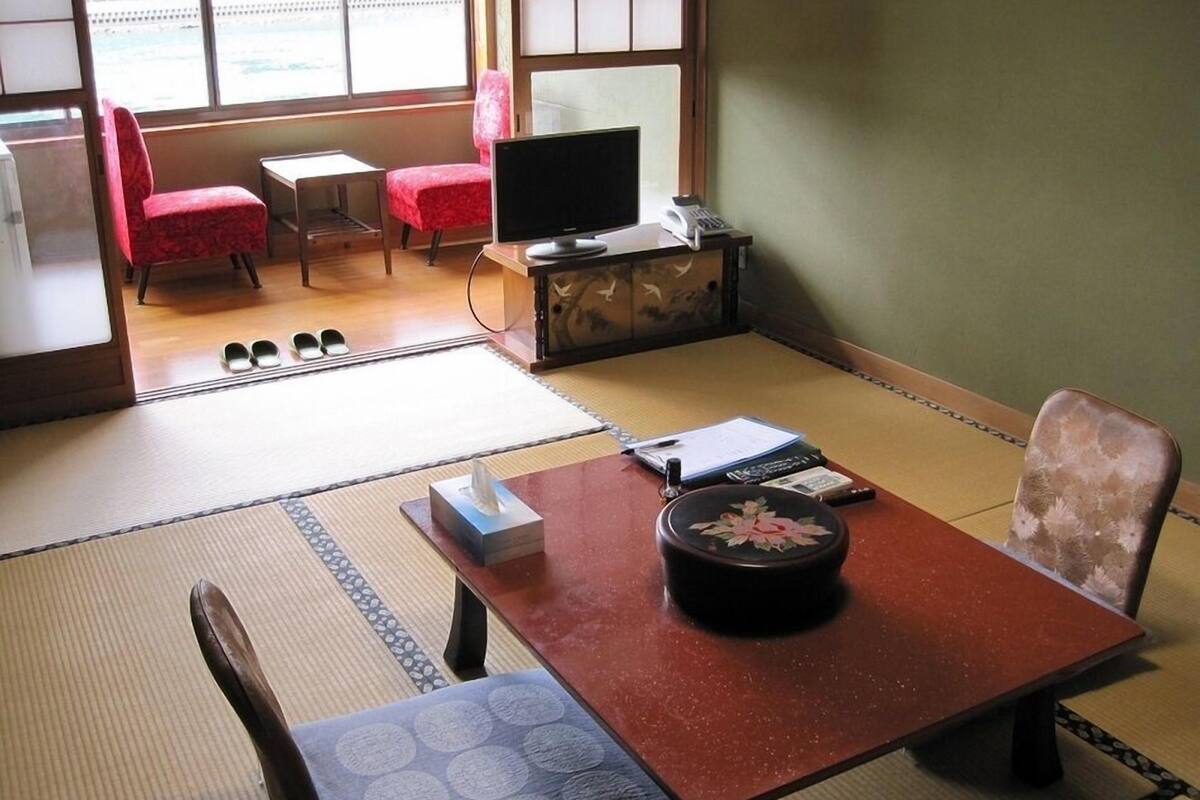 Una habitación de estilo japonés tradicional con suelo de tatami, una mesa baja de tatami, un televisor, un armario y una silla roja.