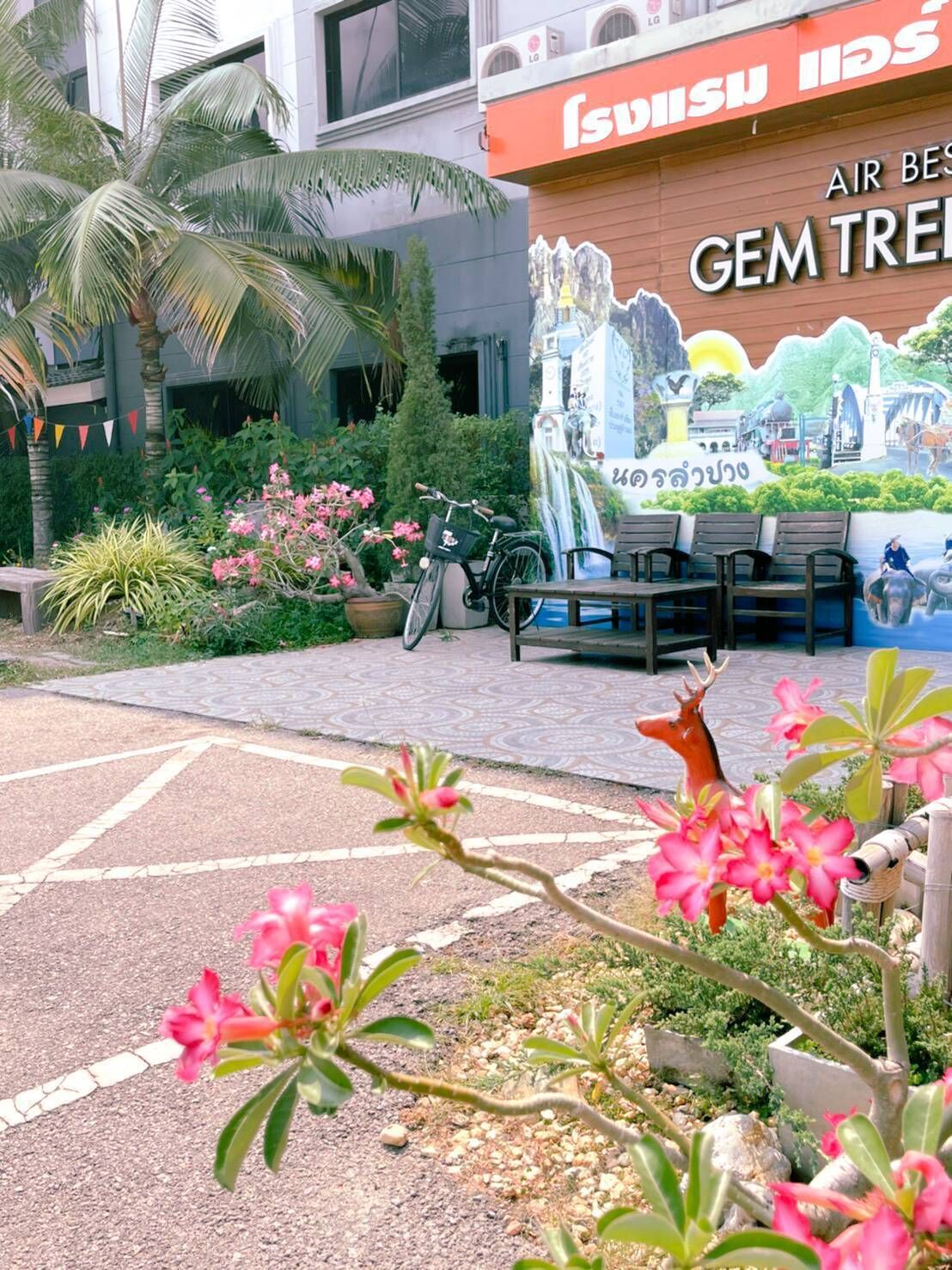 A mural of a scenic landscape with a bicycle and benches, palm trees, and pink flowers in a garden area.