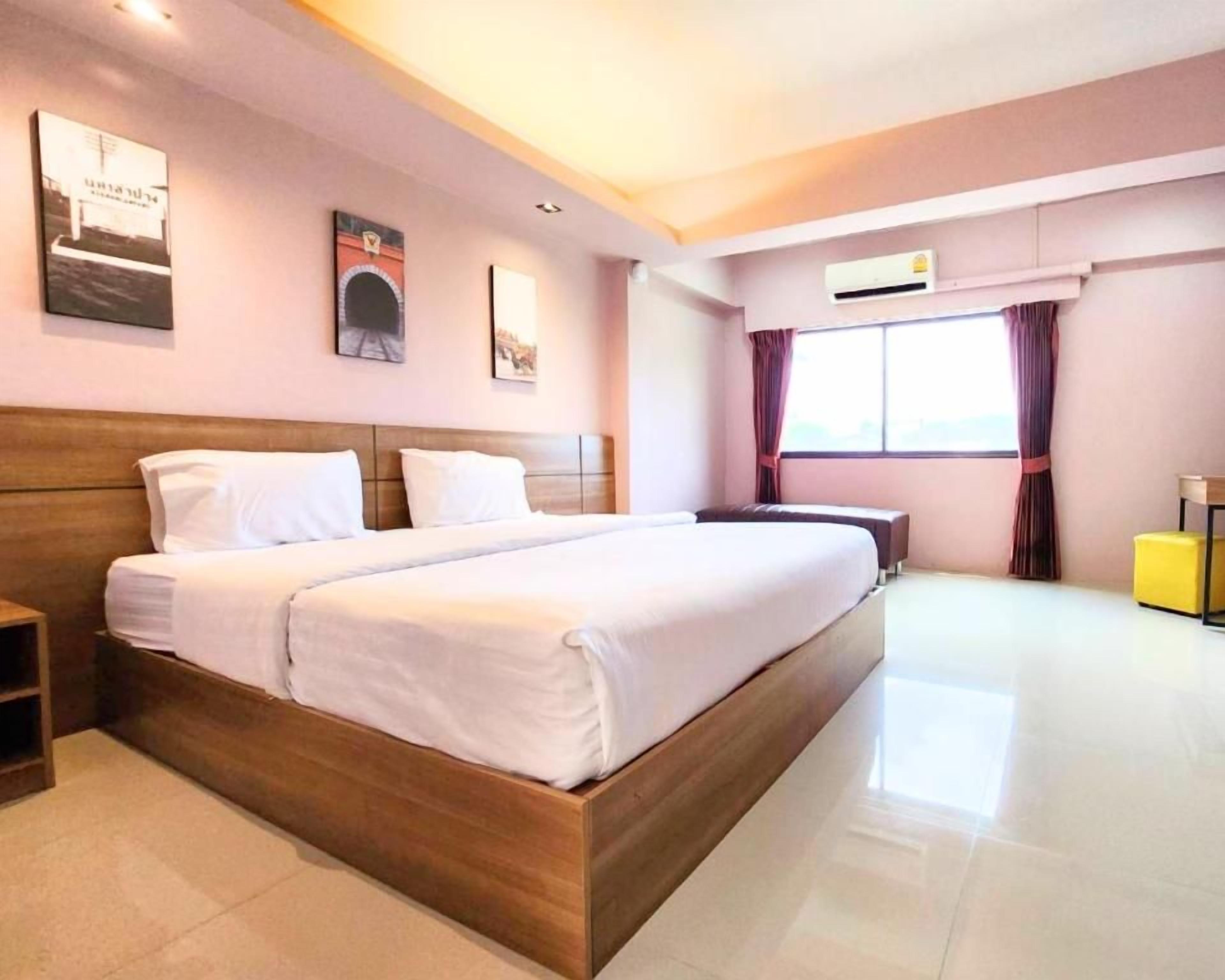 A hotel room with a large bed, a bedside table, a desk, and a window with curtains.