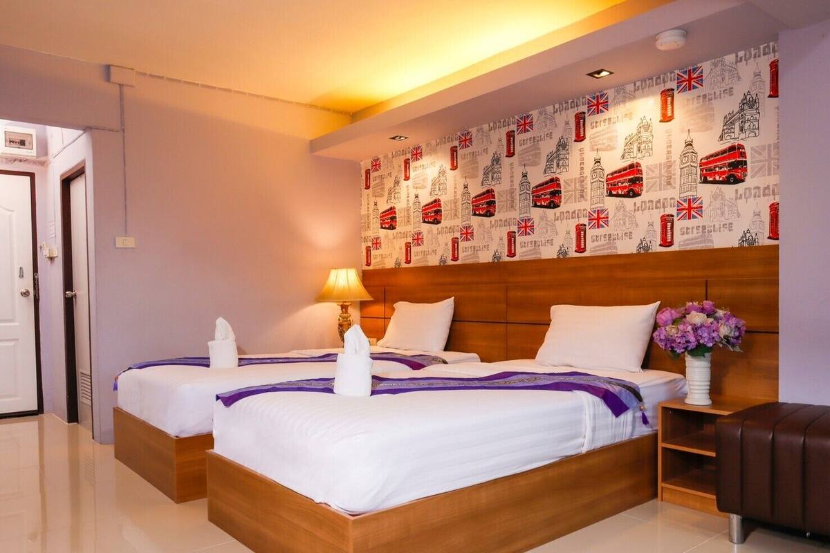 Habitación de hotel con dos camas, cabecero de madera, mesita de noche con un jarrón de flores y un muro decorado con monumentos de Londres.