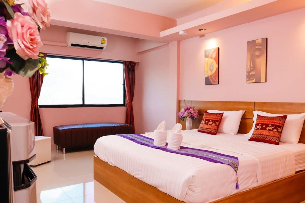 Una habitación de hotel con una cama, un banco, un escritorio y un equipo de aire acondicionado.