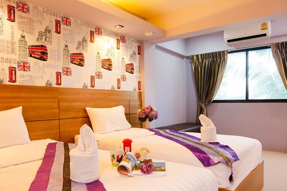 Habitación de hotel con dos camas, una pared decorada con monumentos de Londres, una ventana con cortinas y un equipo de aire acondicionado.