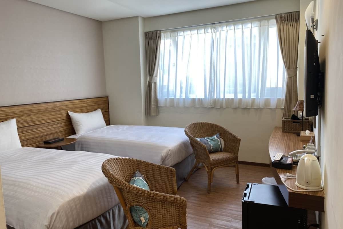 A hotel room with two beds, a desk with a telephone, a television, and wicker chairs.