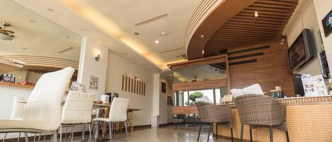 A modern cafe with white leather chairs, a wooden counter, and a large mirror.