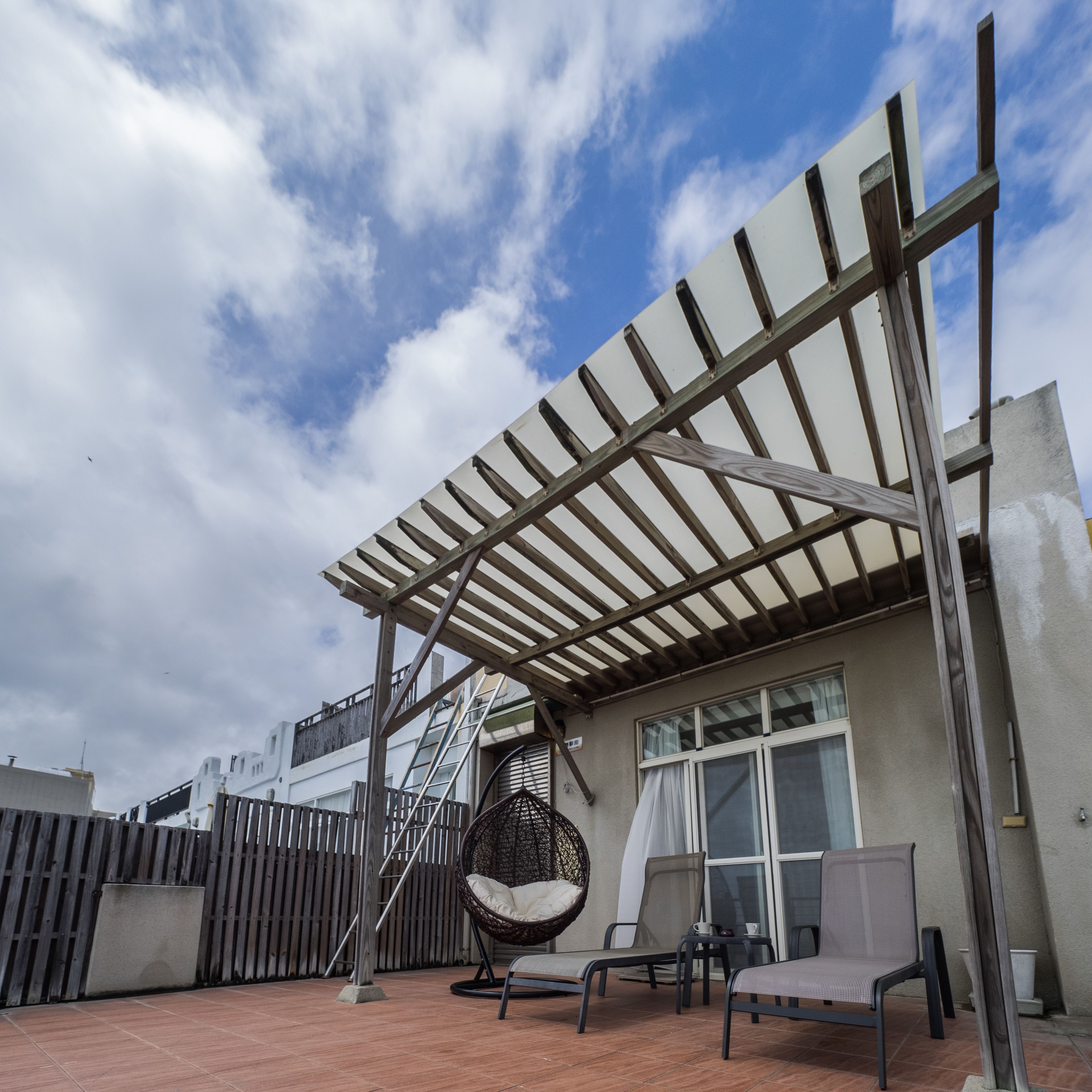 A covered outdoor seating area with a pergola, a hanging chair, and a table with chairs.