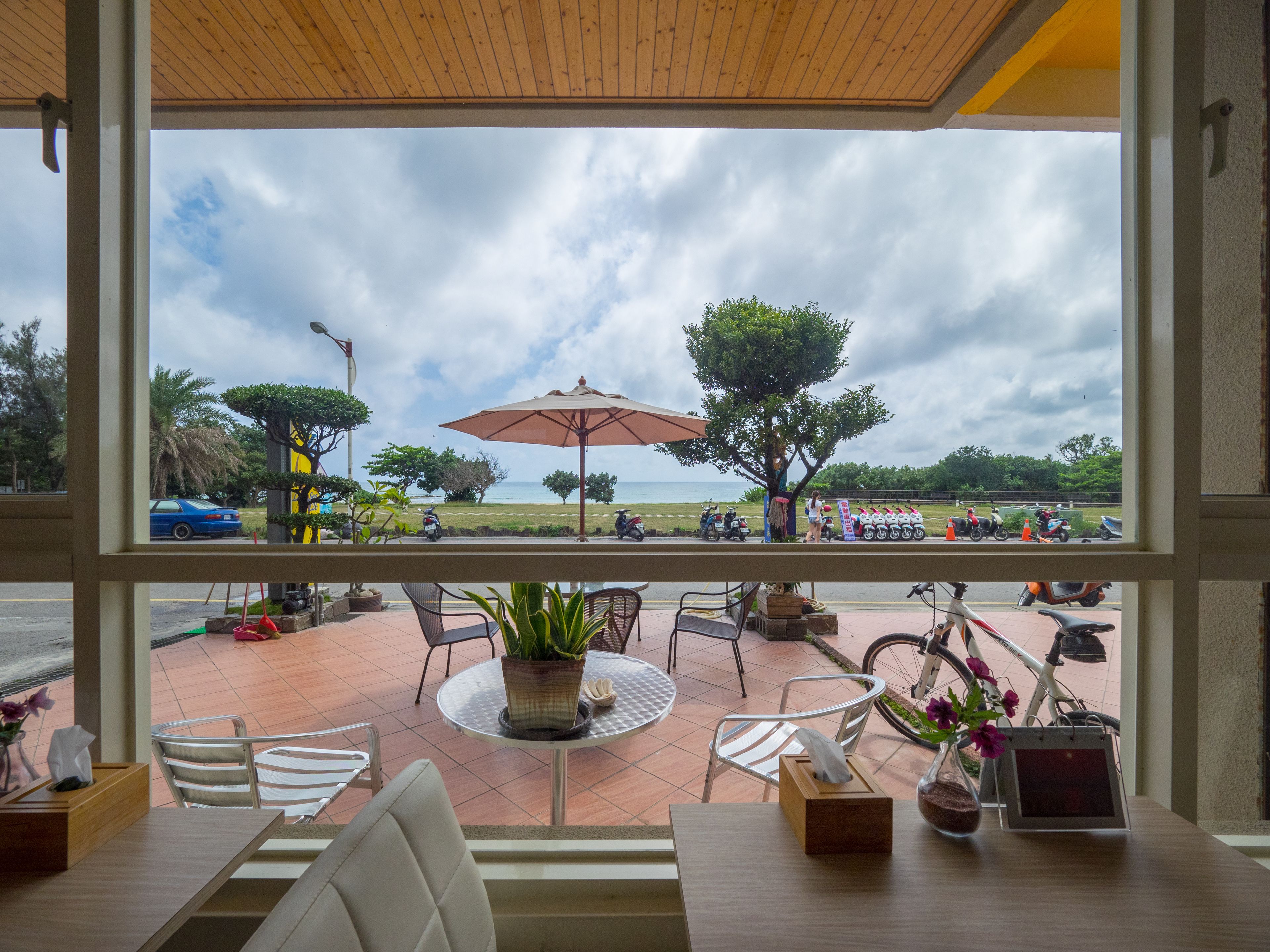 Um terraço de restaurante com mesas ao ar livre, vista para o mar e uma fileira de scooters estacionados.