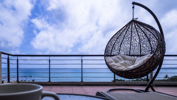 A balcony with a hanging chair and a table, overlooking the ocean. - LoveSea 126 House Inn (Hengchun)