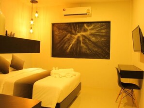 A hotel room with a bed, a desk, a chair, a wall-mounted air conditioner, and a large abstract painting.