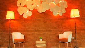 Una habitación con dos sillas blancas, una mesita de madera con una planta, y una pared decorada con lámparas circulares.