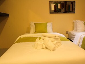 A hotel room with two beds, each with white and green bedding. There is a folded towel on the bed in the foreground.