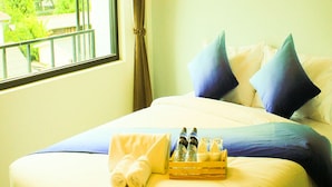 Una cama bien tendida con ropa de cama azul y blanca, una ventana con vistas a la vegetación y una bandeja con artículos de aseo.