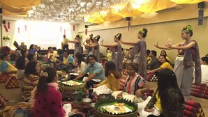 Una habitación con mesas dispuestas para una comida, personas sentadas y un grupo bailando.