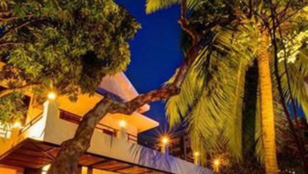 A pool area with a covered seating area, surrounded by palm trees and a building with a balcony. - Base Villa Phnom Penh - Hostel (Phnom Penh)