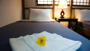 A neatly made bed with a white towel and a yellow flower on it, a lamp on a bedside table, and a window with blinds in a hotel room. - Base Villa Phnom Penh - Hostel (Phnom Penh)