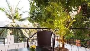 A balcony with a metal railing, a wicker chair, a potted plant, and a table with a glass of water and a small vase. - Base Villa Phnom Penh - Hostel (Phnom Penh)