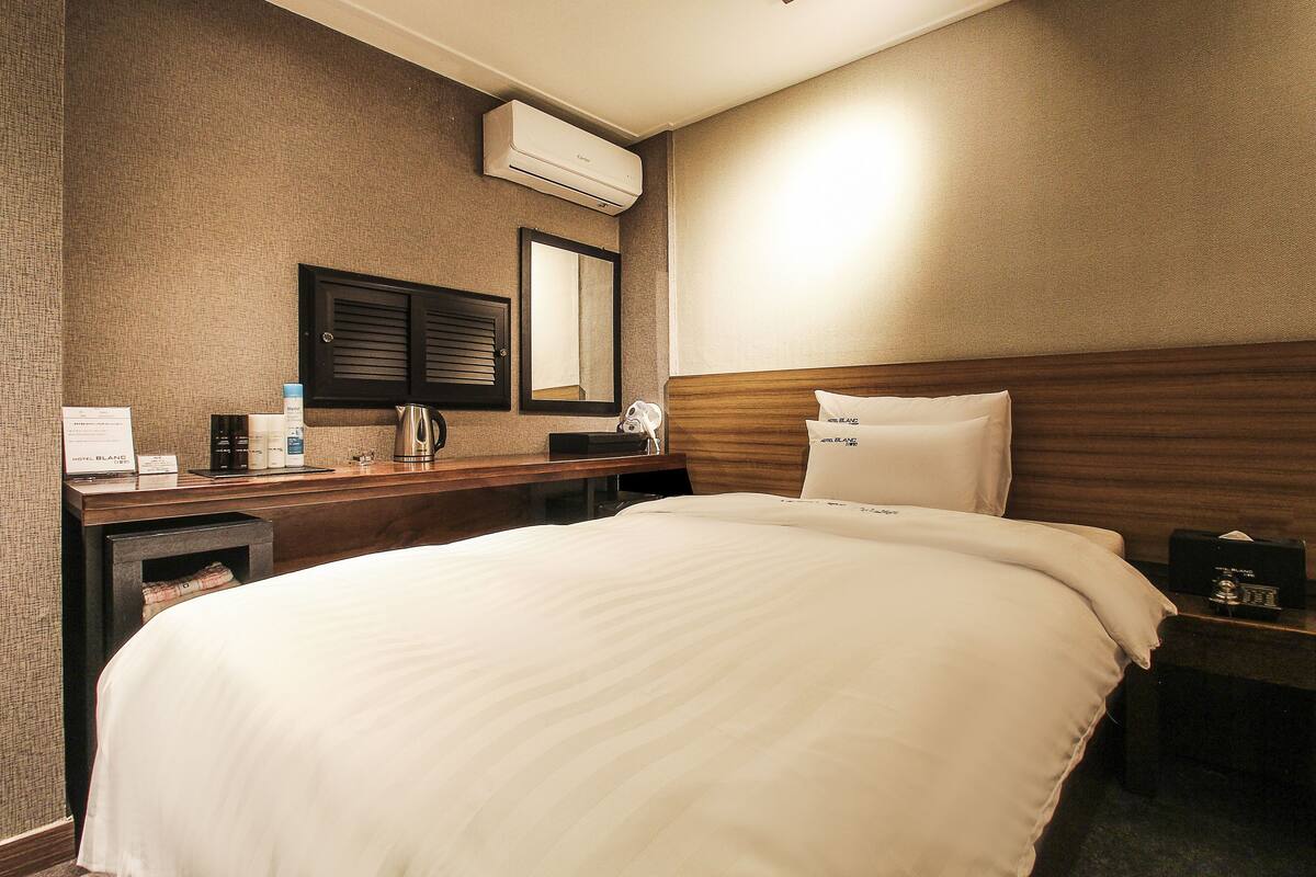 Une chambre d’hôtel avec un grand lit, une tête de lit en bois, une table de chevet avec une lampe, un miroir et un climatiseur fixé au mur.