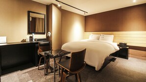 Hotellihuone, jossa on sänky, yöpöytä, tuoli, työpöytä ja peili.