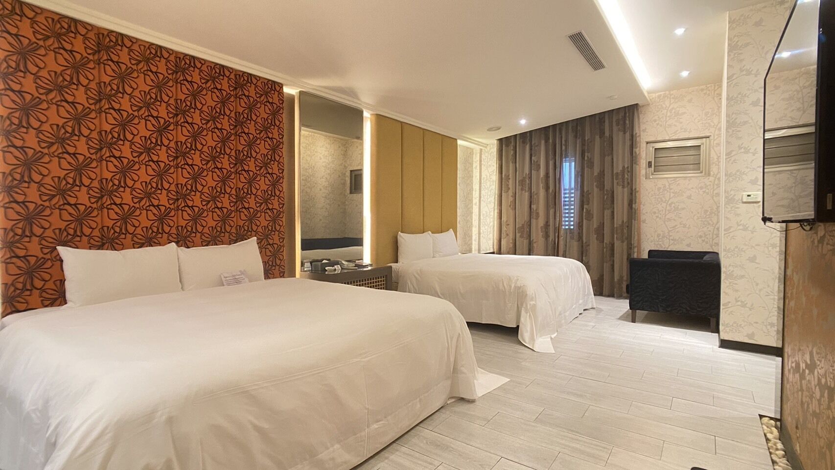 Une chambre d’hôtel avec deux lits, un miroir, une télévision et un coin salon.