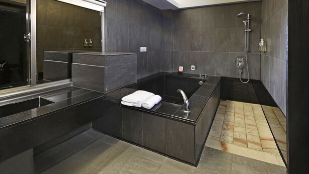 Un baño moderno con una bañera negra grande, una zona de ducha separada y un inodoro con cerramiento de vidrio.