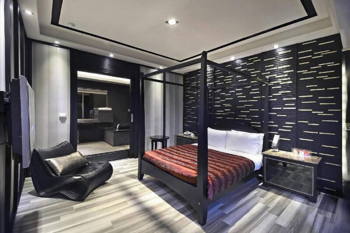A modern bedroom with a four-poster bed, a seating area, a vanity, and a walk-in closet.