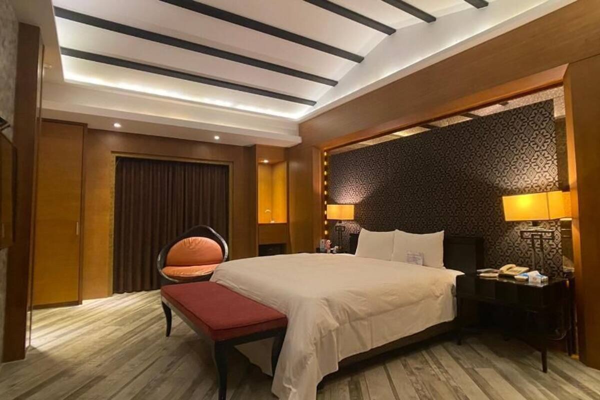 A hotel room with a bed, bedside table, lamp, and a chair.