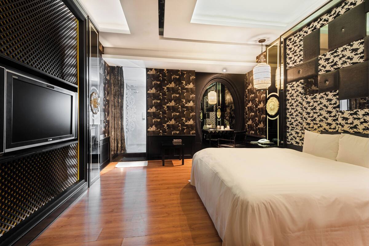 A modern hotel room with a large bed, a desk, a television, and a decorative mirror.