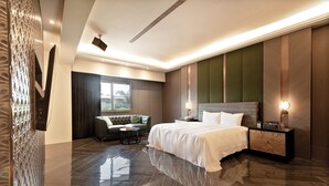 Una habitación de hotel moderna con una cama grande, un sofá, una mesita y una mesita de noche con una lámpara.